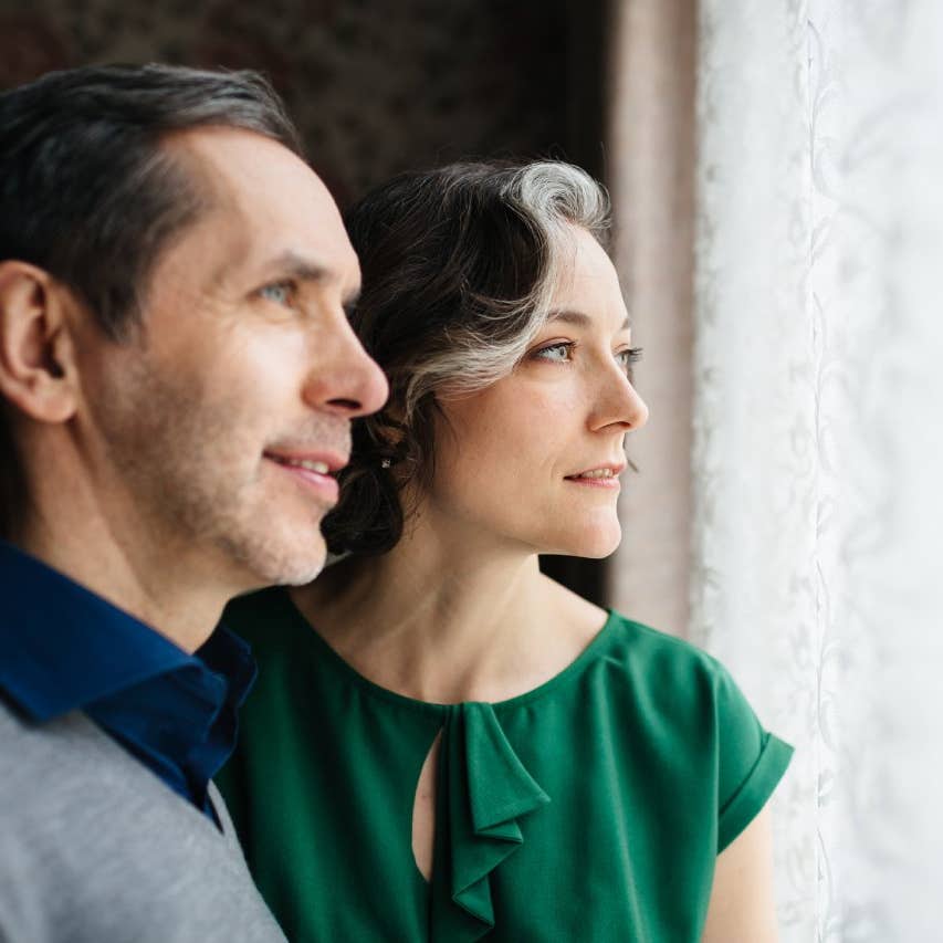 A mature couple is looking out of a bright window.